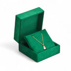 Gold necklace with a pendant in an open green square-shaped jewelry box on a white background